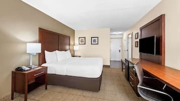 Quarto de hotel com cama, escrivaninha, cadeira, televisão e luminária.