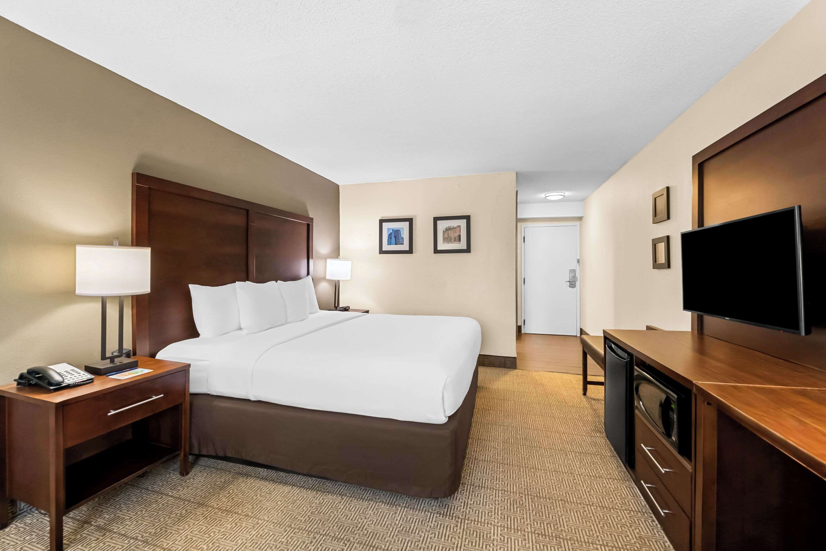 Une chambre d’hôtel avec un grand lit, un bureau avec une lampe, une télévision et une armoire.