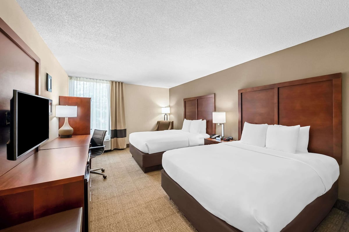 Ein Hotelzimmer mit zwei Betten, einem Fernseher, einem Schreibtisch und einem Stuhl.
