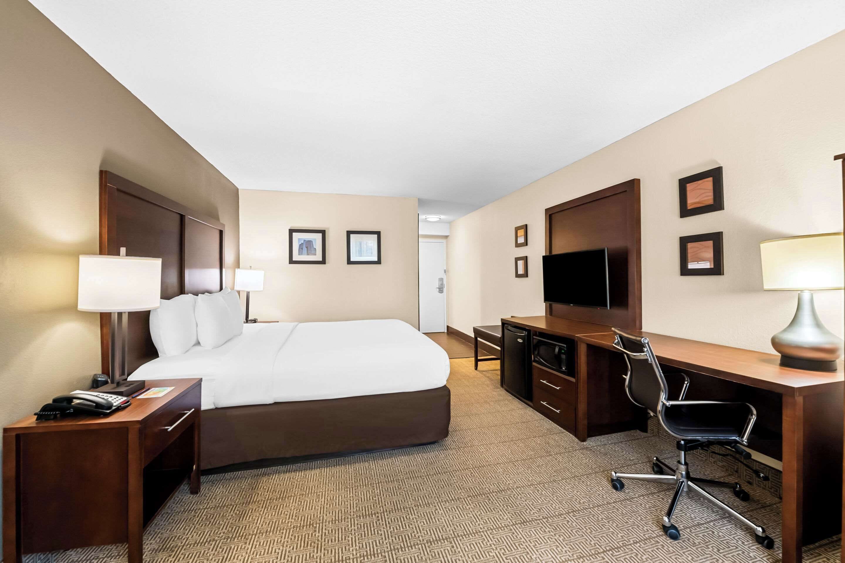 Een hotelkamer met een groot bed, nachtkastjes, een bureau met stoel, een televisie en ingekaderde foto's aan de muur.