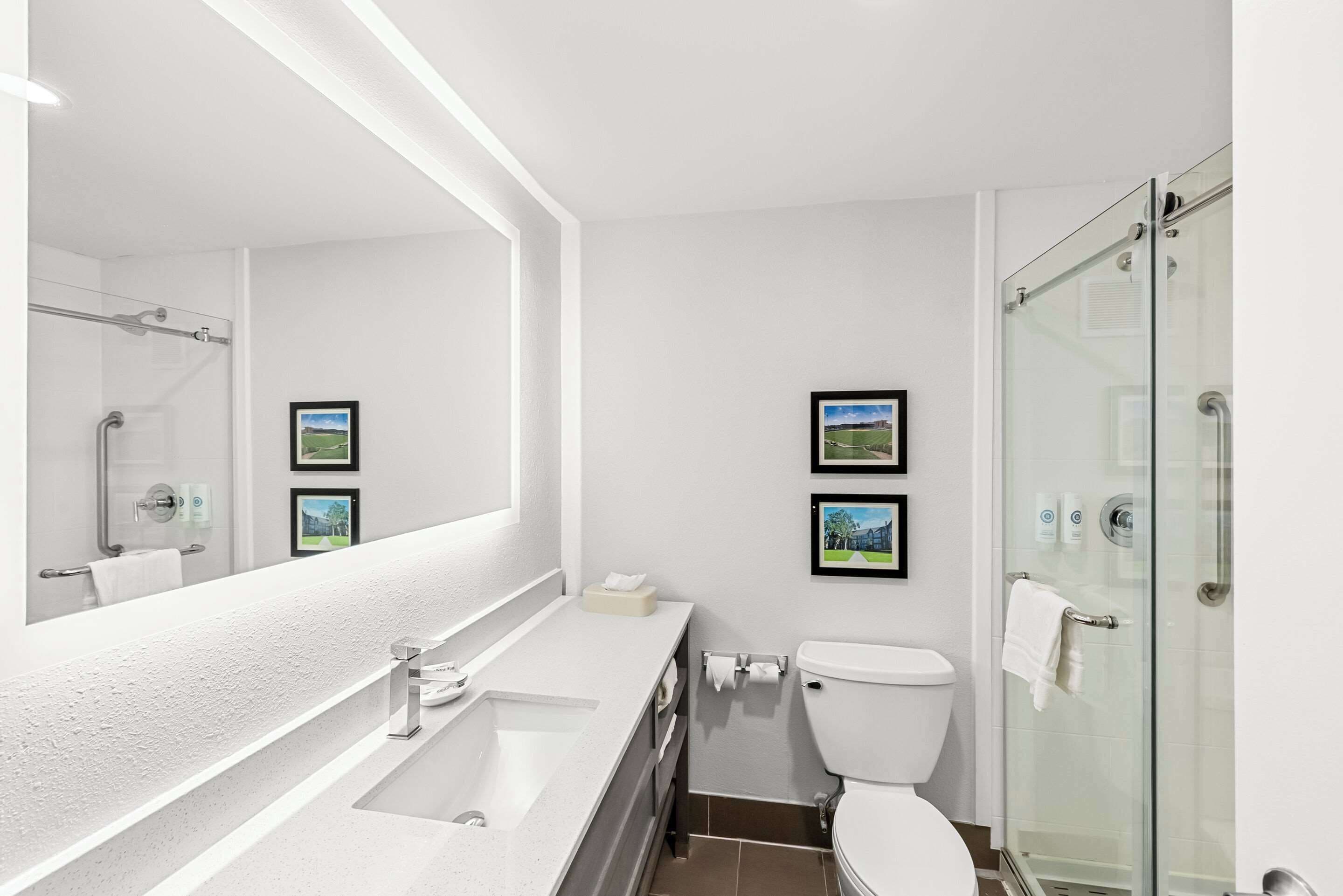 A modern bathroom with a large mirror, a bathtub, a toilet, and a glass shower enclosure.