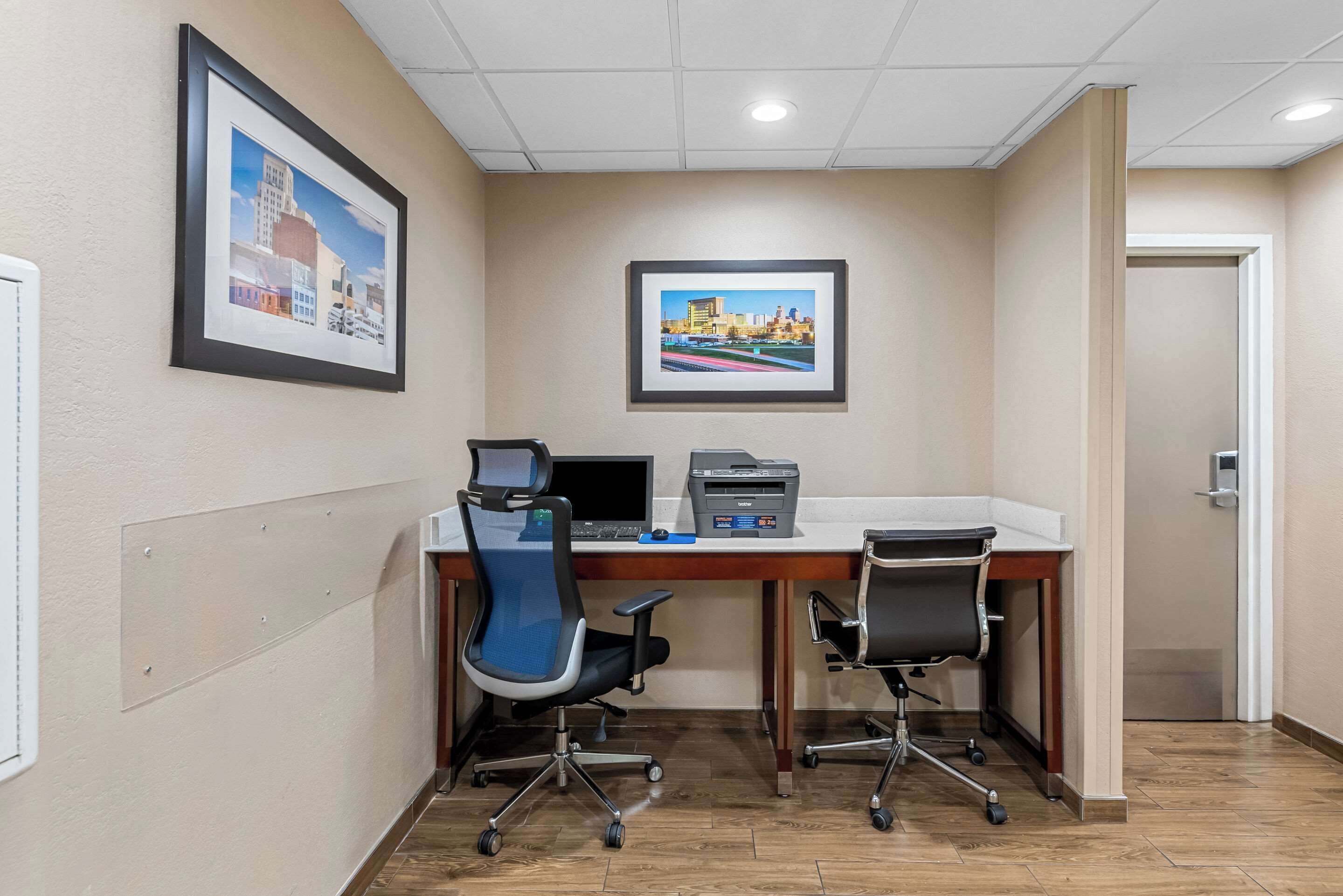 A hotel room with a desk, two office chairs, a printer, and two framed pictures on the wall.