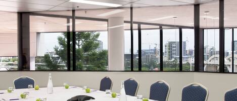 Un salón de conferencias con una larga mesa, sillas y ventanas amplias que ofrecen vistas a la ciudad.