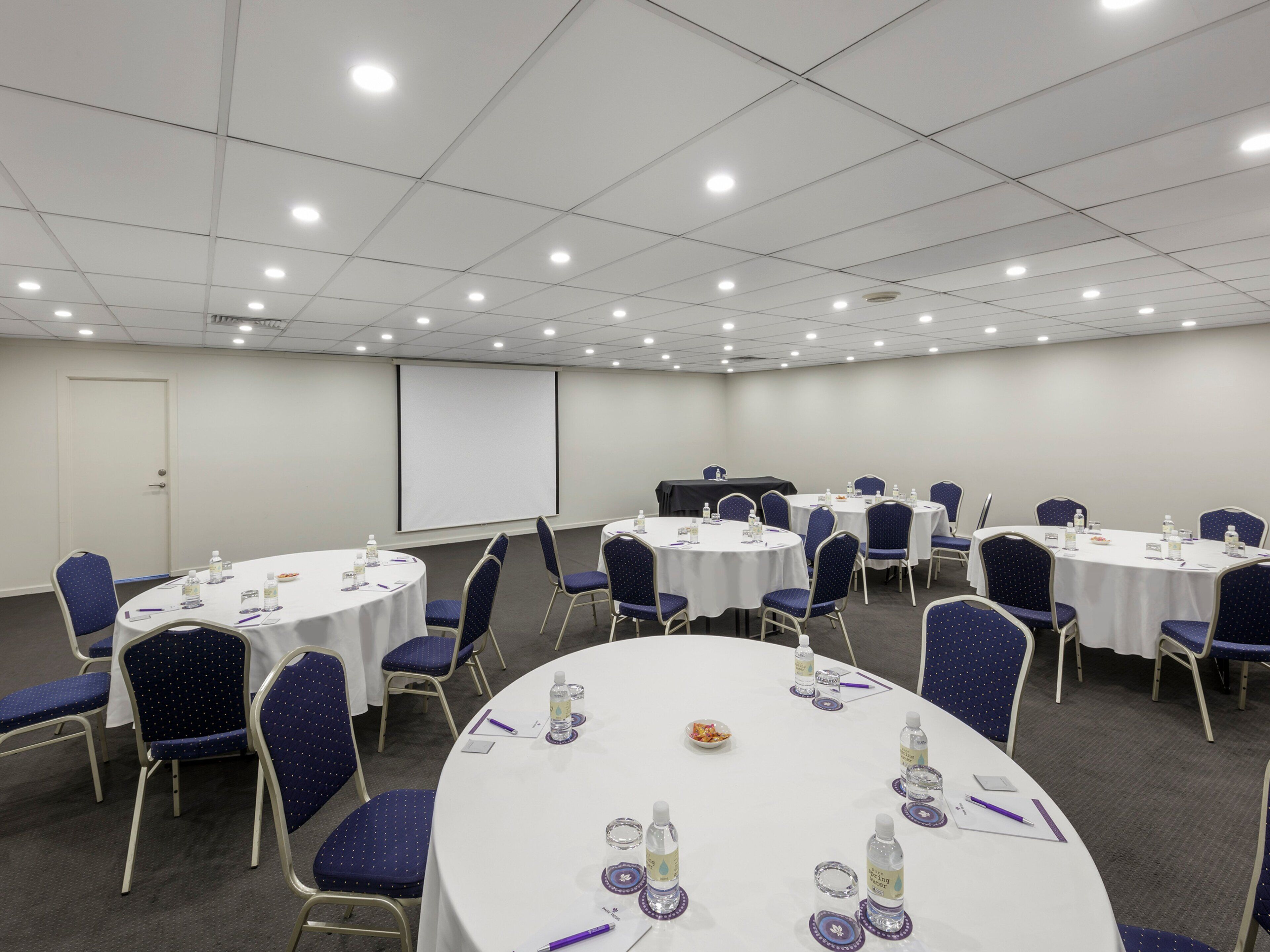 A conference room with round tables, chairs, and a projector screen.