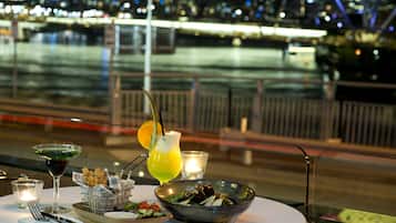 Une table dressée avec une salade, des boissons et une bougie, donnant sur une vue panoramique de la ville la nuit.