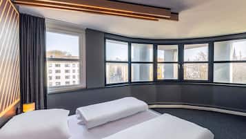 Et hotelværelse med to senge, et stort vindue med udsigt til bygninger, og et moderne loftdesign.