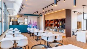 Een modern restaurant met een lange toonbank, witte stoelen en een muurschildering van een stadshemelbeeld.