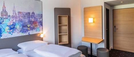 Een hotelkamer met twee bedden, een stadsgezicht schilderij, een houten plank, een wandlamp en een deur.