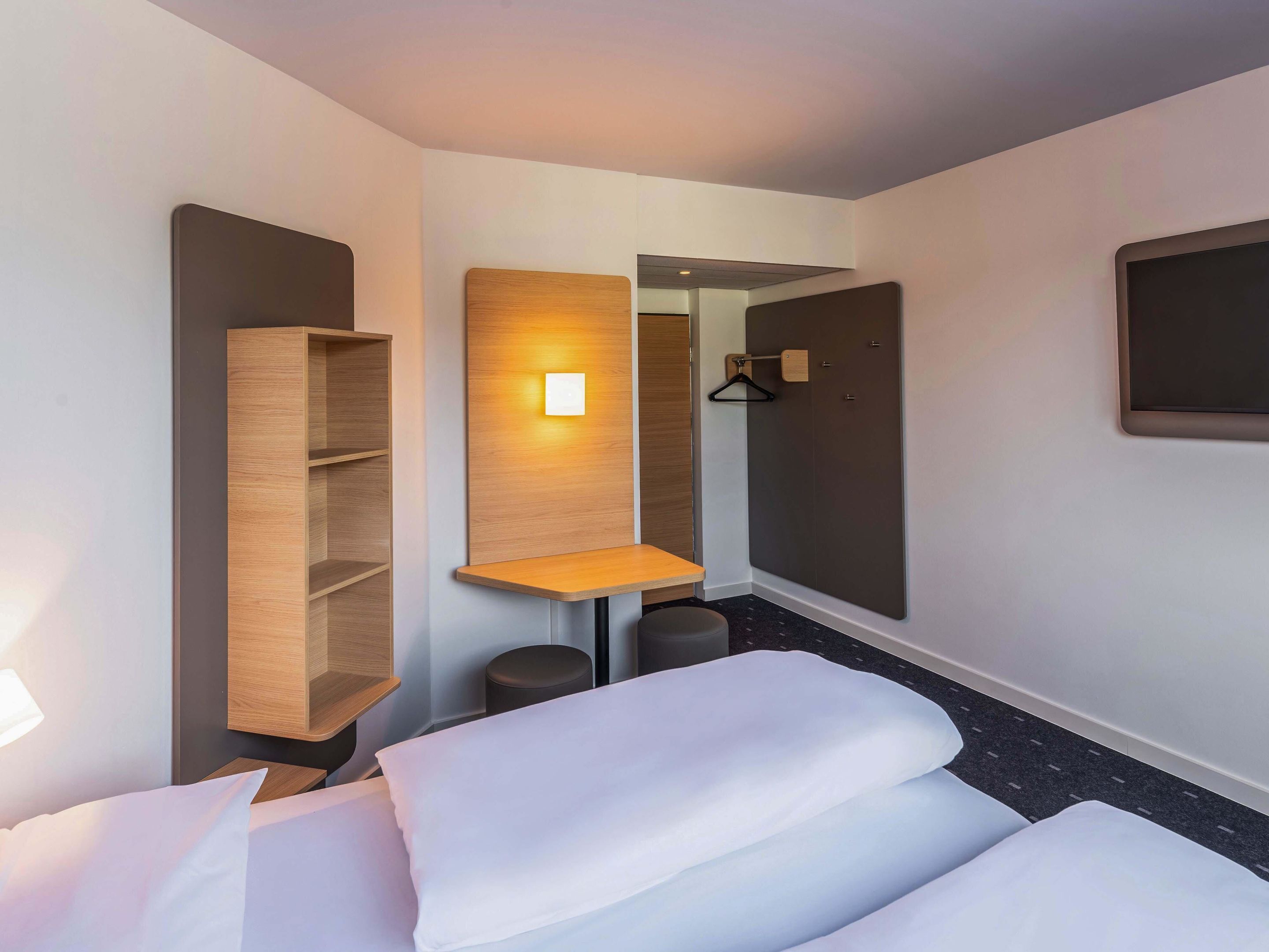Ein Hotelzimmer mit einem Bett, einer Holzregaleinheit, einem kleinen Tisch, einem Hängekleiderständer und einem Spiegel.