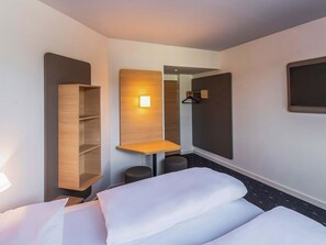Une chambre d’hôtel comprenant un lit, une étagère en bois, une petite table, un porte-manteau mural et un miroir.