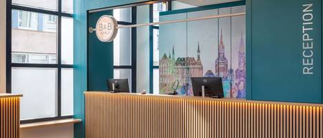 Un espace d’accueil au design moderne, comprenant un comptoir d’accueil en bois, une fresque représentant un paysage urbain et un panneau indiquant la réception.