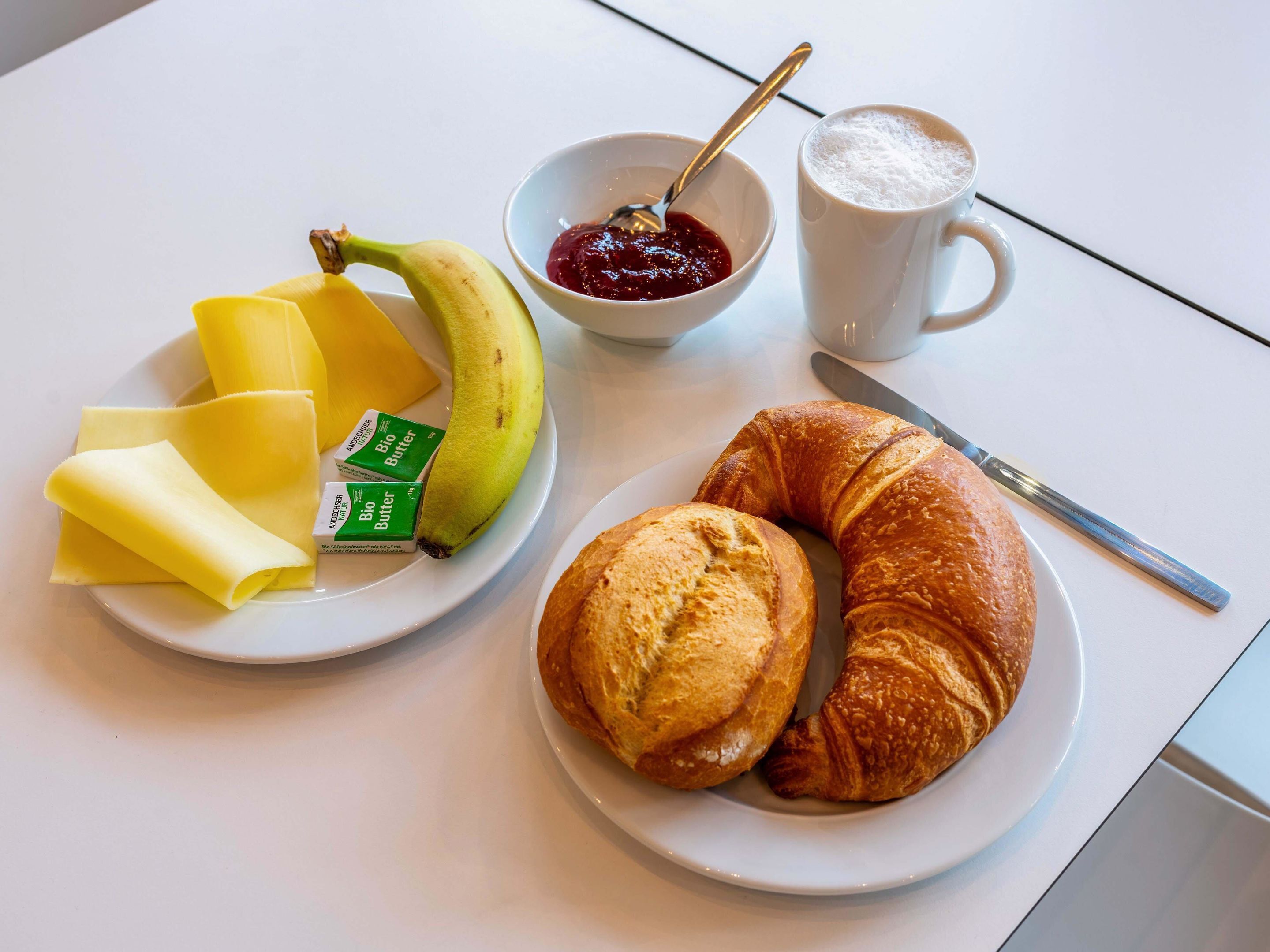 A plate with a banana, a croissant, and a bowl of jam.