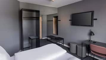 Ein modernes Hotelzimmer mit Bett, Schreibtisch, Stuhl, Kleiderschrank, Spiegel und Fernseher.