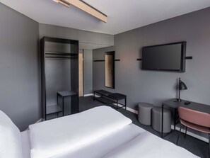 Une chambre d’hôtel moderne équipée d’un lit, d’un bureau, d’une chaise, d’une armoire, d’un miroir et d’une télévision.
