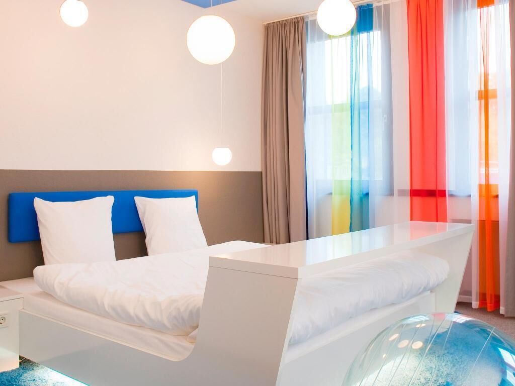 Een moderne hotelkamer met een bed, nachtkastje en een bolvormig object in een glazen behuizing.