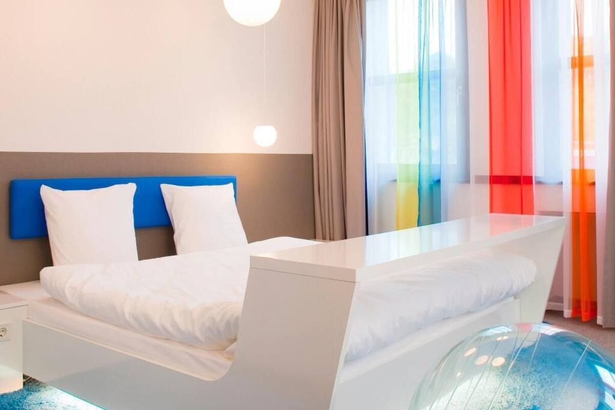 Une chambre d’hôtel moderne avec un lit, une table de chevet et un objet sphérique contenu dans une structure de verre.