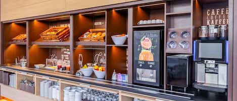 Un café moderne, doté d’une machine à café, d’un présentoir de fruits, ainsi que de tasses et de bols disposés avec soin.