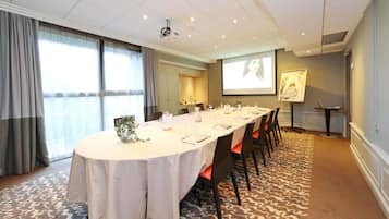 Un salón de conferencias con una larga mesa, sillas, una pantalla de proyector y un amplio ventanal.