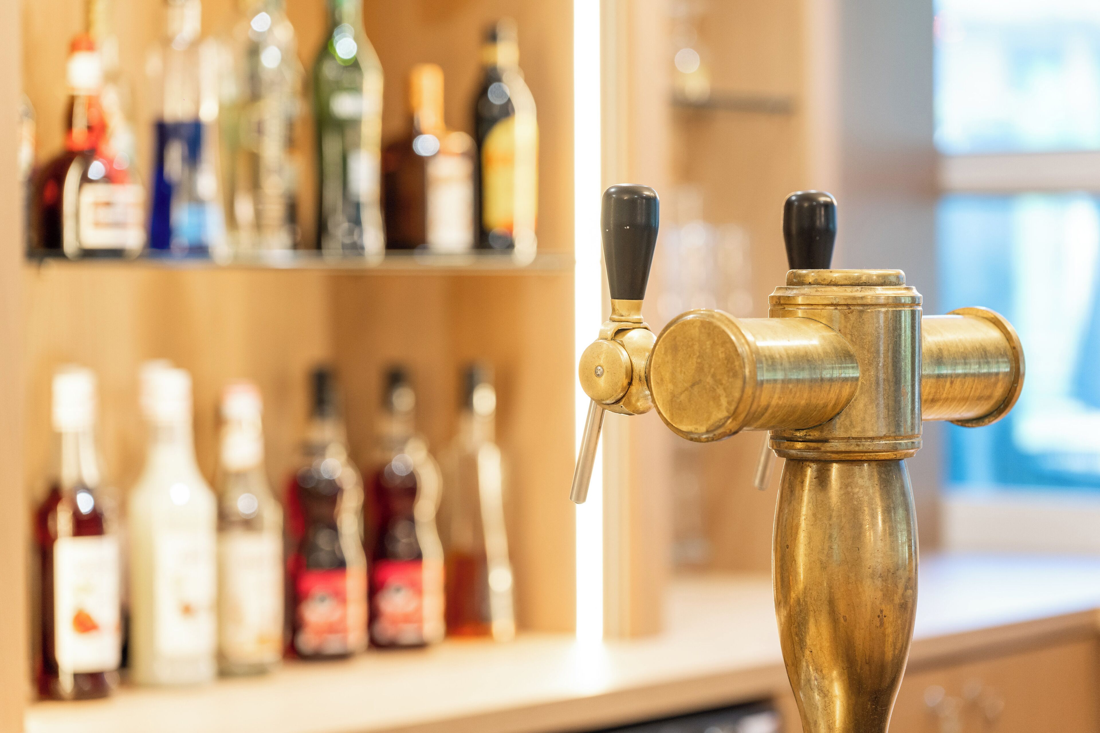 Un grifo de bronce con dos mandos, situado frente a una estantería con varias botellas.