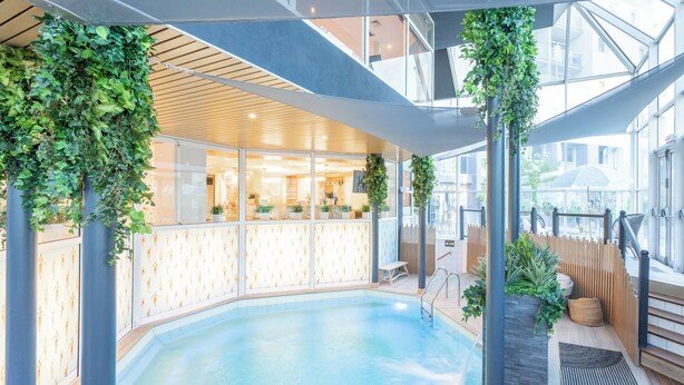 Una piscina interior con cubierta de madera, paredes de vidrio y plantas verdes.