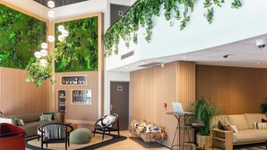 Un vestíbulo moderno con una pared verde, paneles de madera y diversas opciones de asientos, incluyendo un sofá, sillas y un carrito rojo.