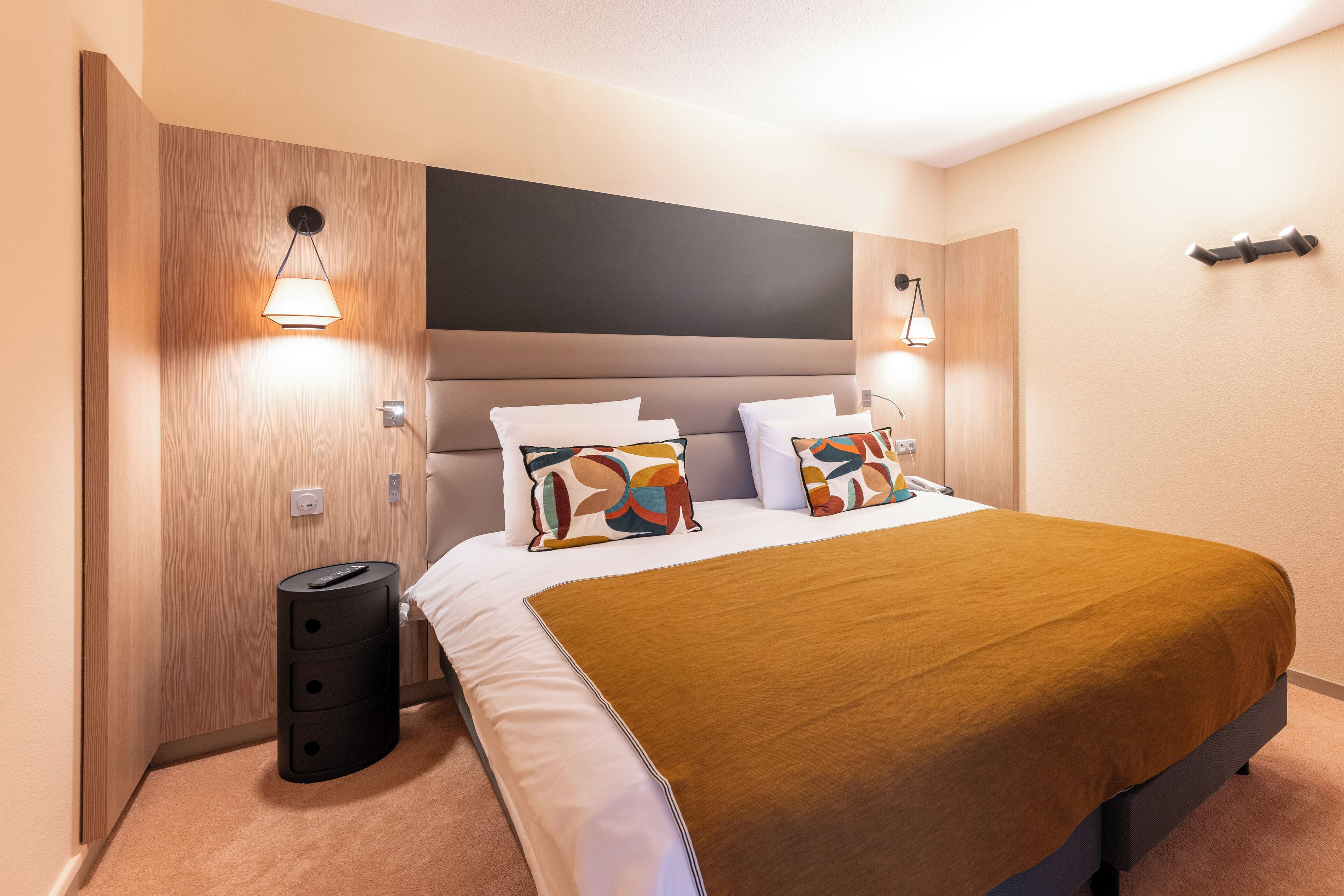 A modern hotel room with a large bed, a headboard, and two bedside lamps.