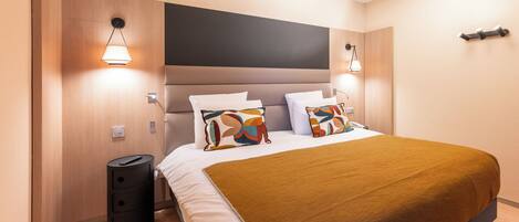 A modern hotel room with a large bed, a headboard, and two bedside lamps.