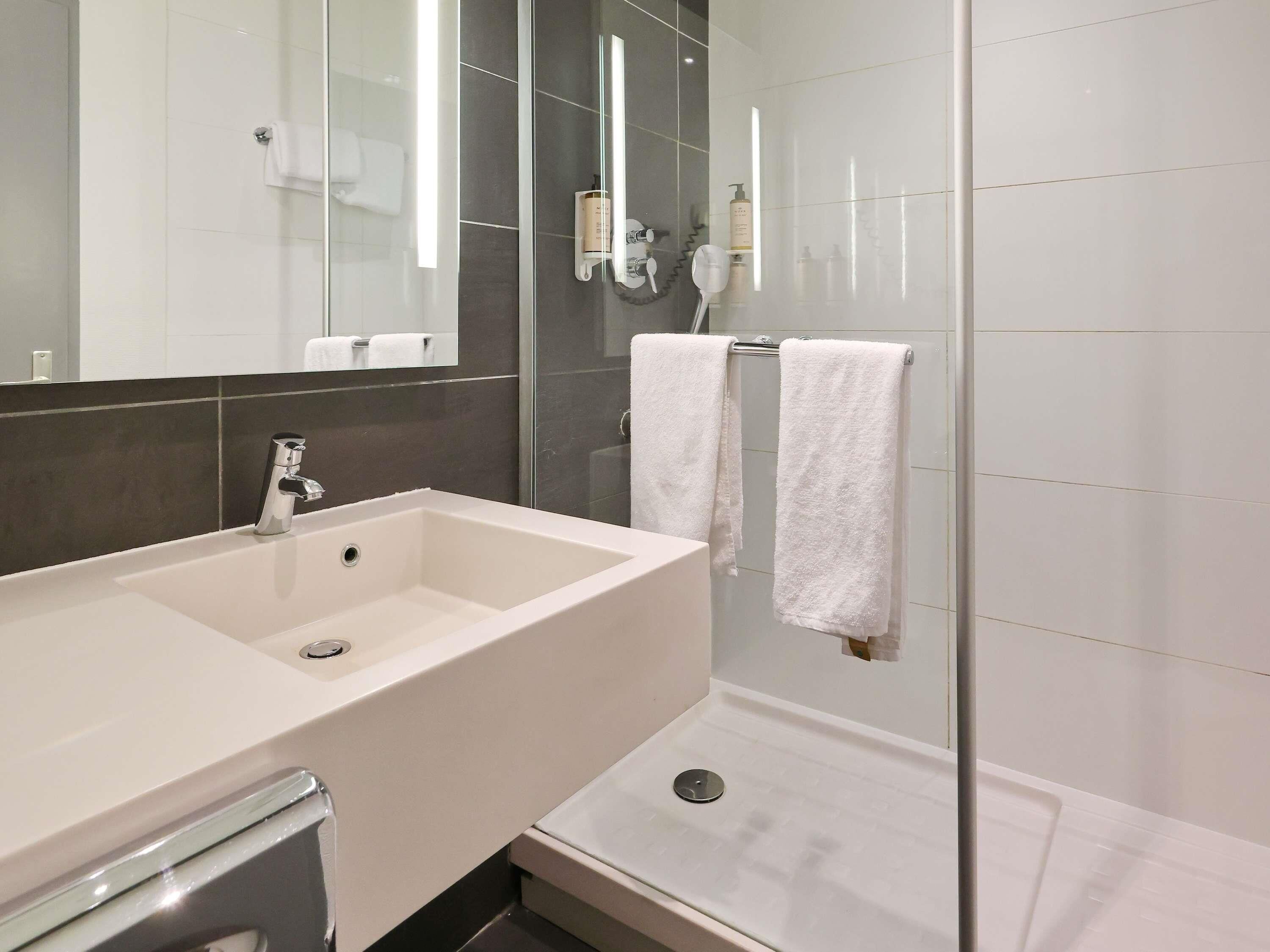 A modern bathroom with a large white sink, a glass shower enclosure, and a mirror.