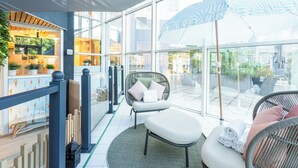 Un interior moderno con paredes de vidrio, una silla de mimbre, un banco acolchado y un paraguas estampado.