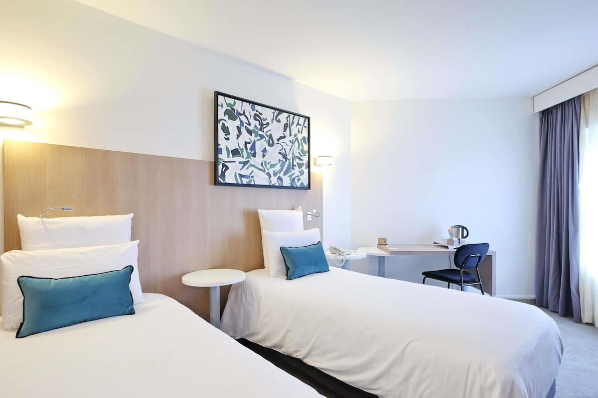 Una habitación de hotel con dos camas, un escritorio, una silla y un cuadro en la pared.