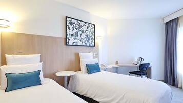 Une chambre d’hôtel avec deux lits, un bureau, une chaise et un tableau au mur.