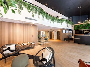 Eine Hotelhalle mit Empfangstresen, einer Sitzecke und einer Wand mit hängenden Pflanzen.