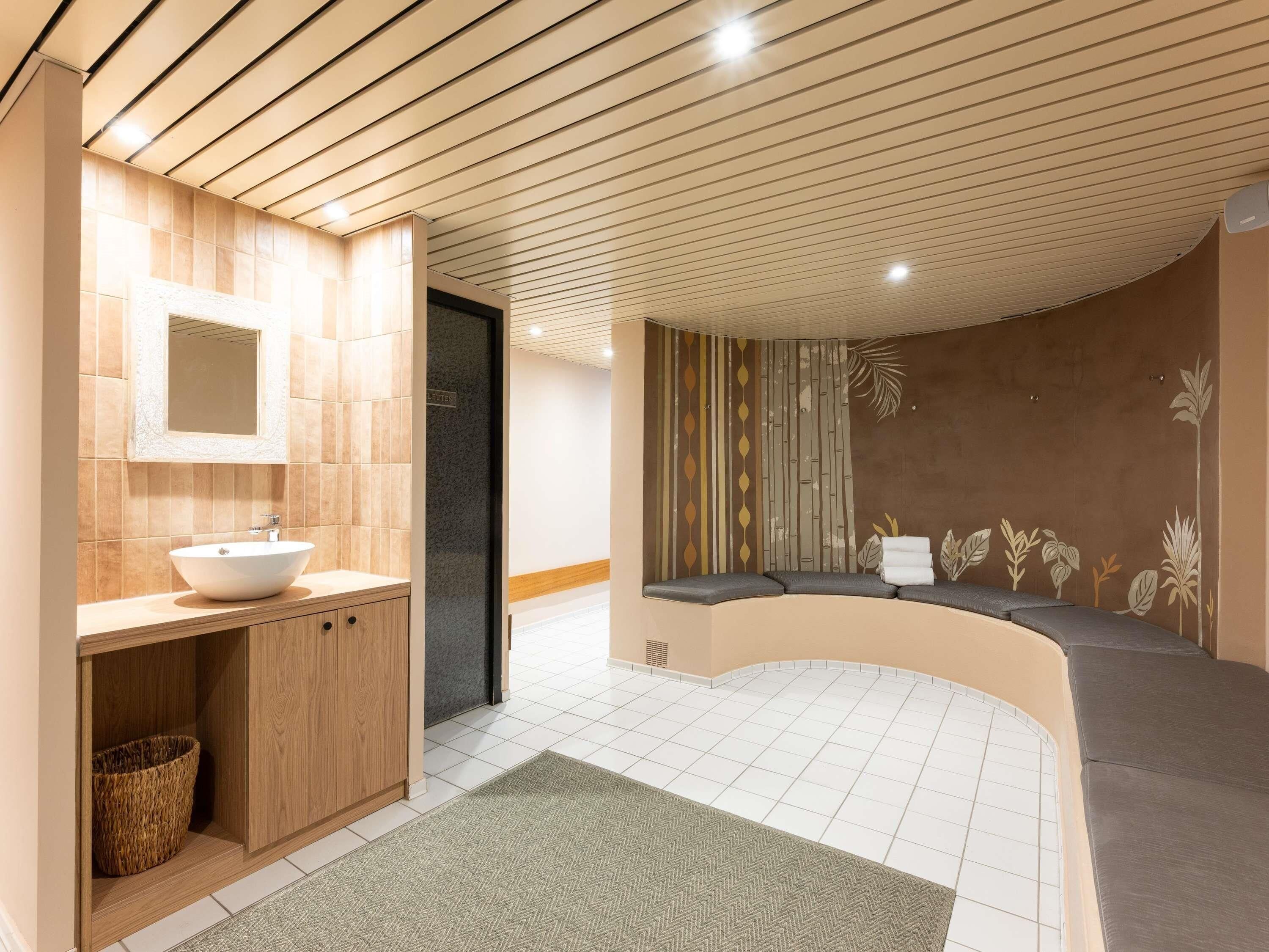 Une salle de bain moderne avec un meuble-lavabo en bois, un grand miroir et un coin salon agrémenté d’une fresque murale.