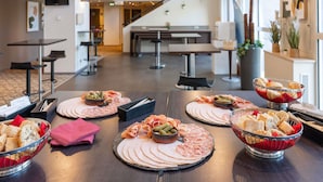 Montaje tipo bufé con diferentes carnes, quesos y pan en un moderno hotel.