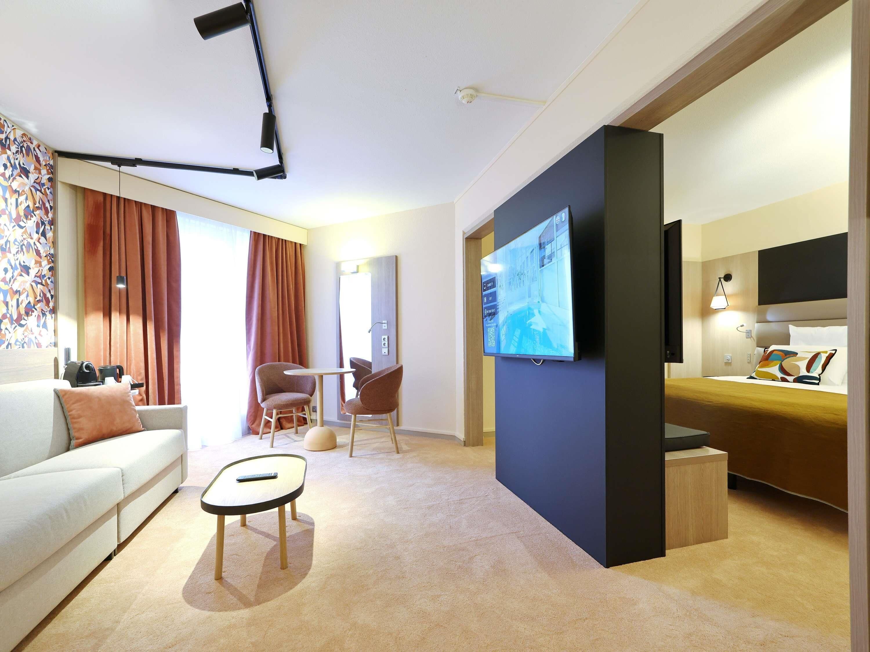 Een moderne hotelkamer met een flatscreen televisie, een bank, een klein tafeltje en een bed met hoofdeinde.