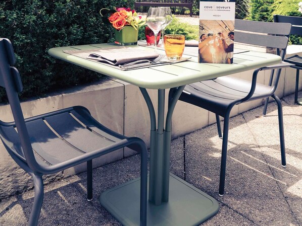 An outdoor table with chairs, a vase of flowers, and a wine glass.
