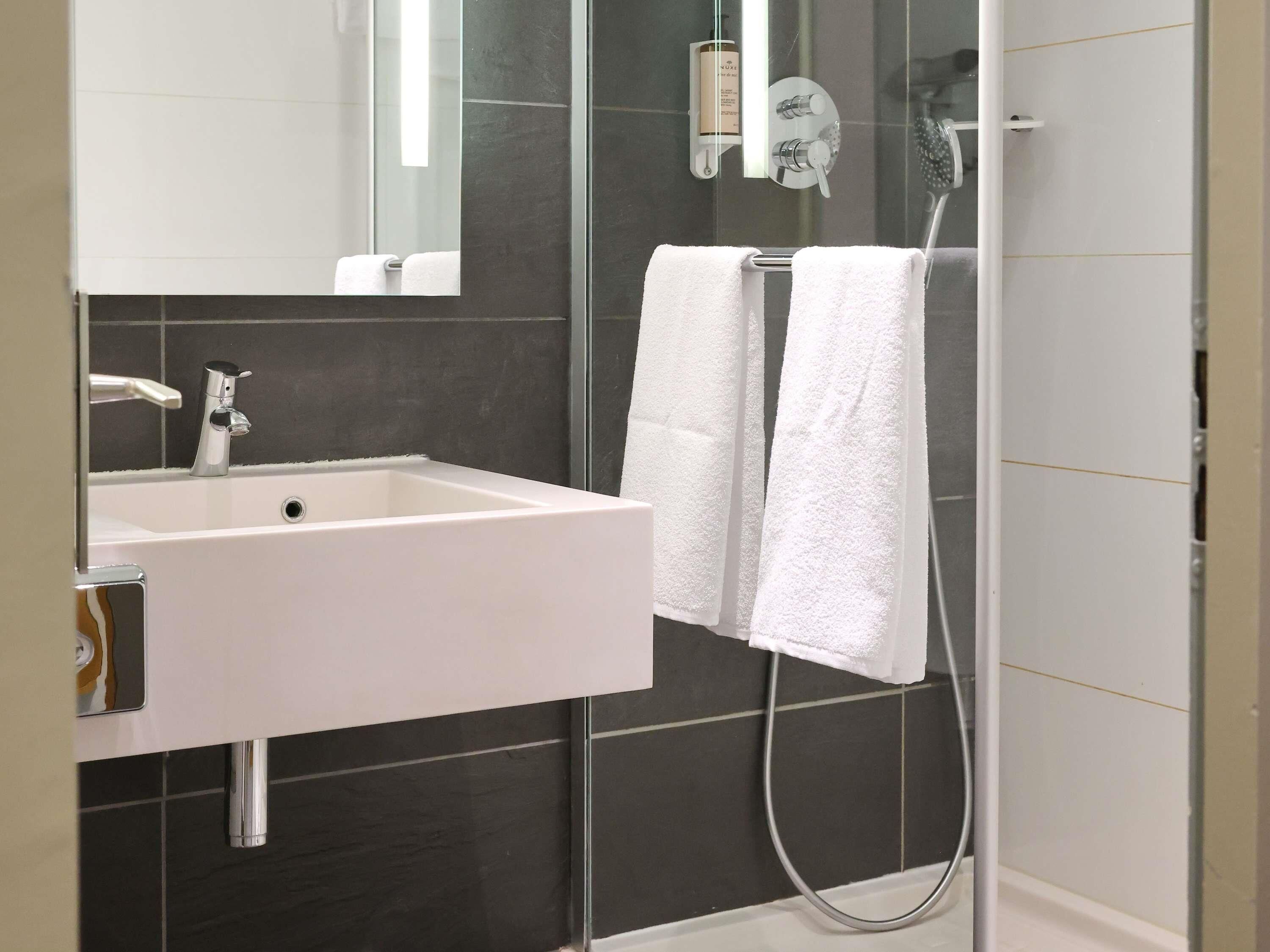 A modern bathroom with a white sink, a glass shower enclosure, and two white towels hanging on a rack.