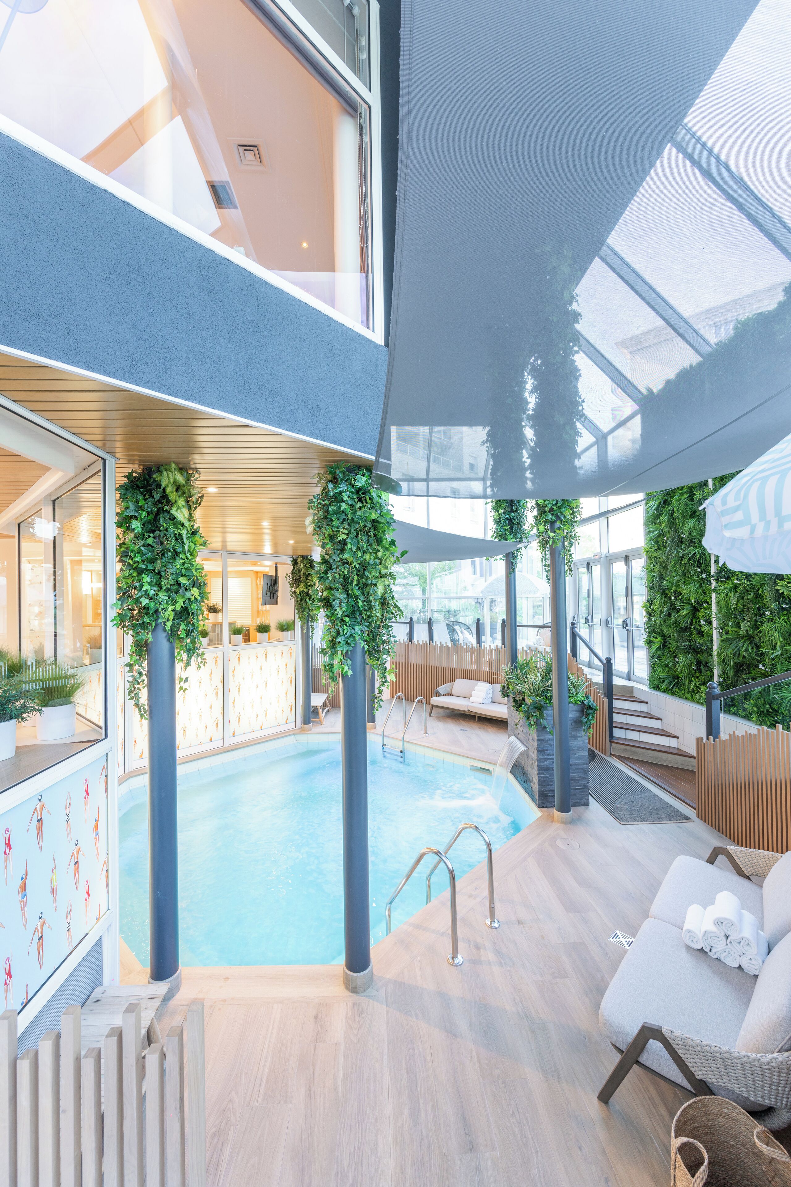 An indoor swimming pool with a wooden deck, lounge chairs, and a glass ceiling.