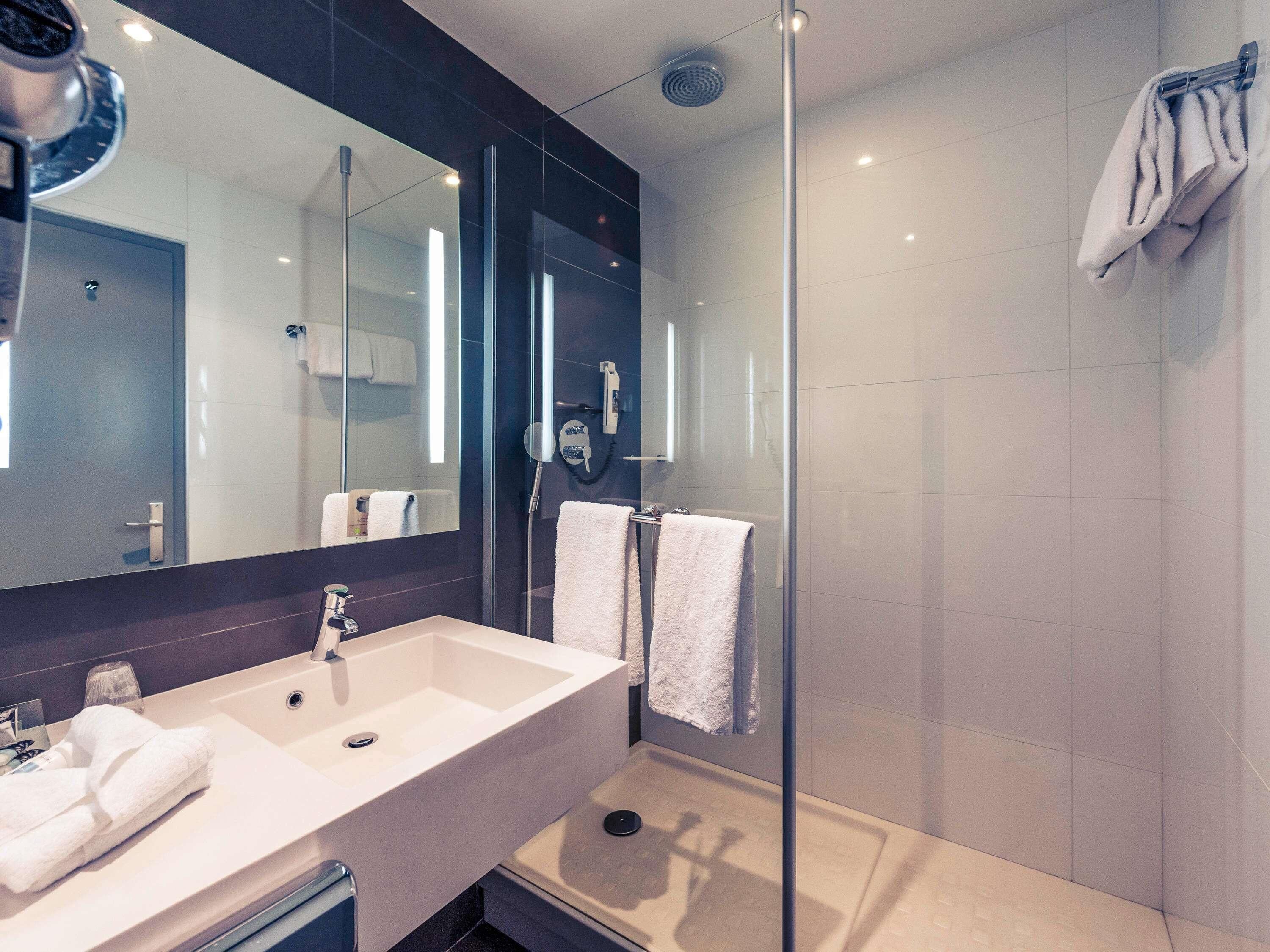 A modern bathroom with a large mirror, a sink, and a glass-enclosed shower.