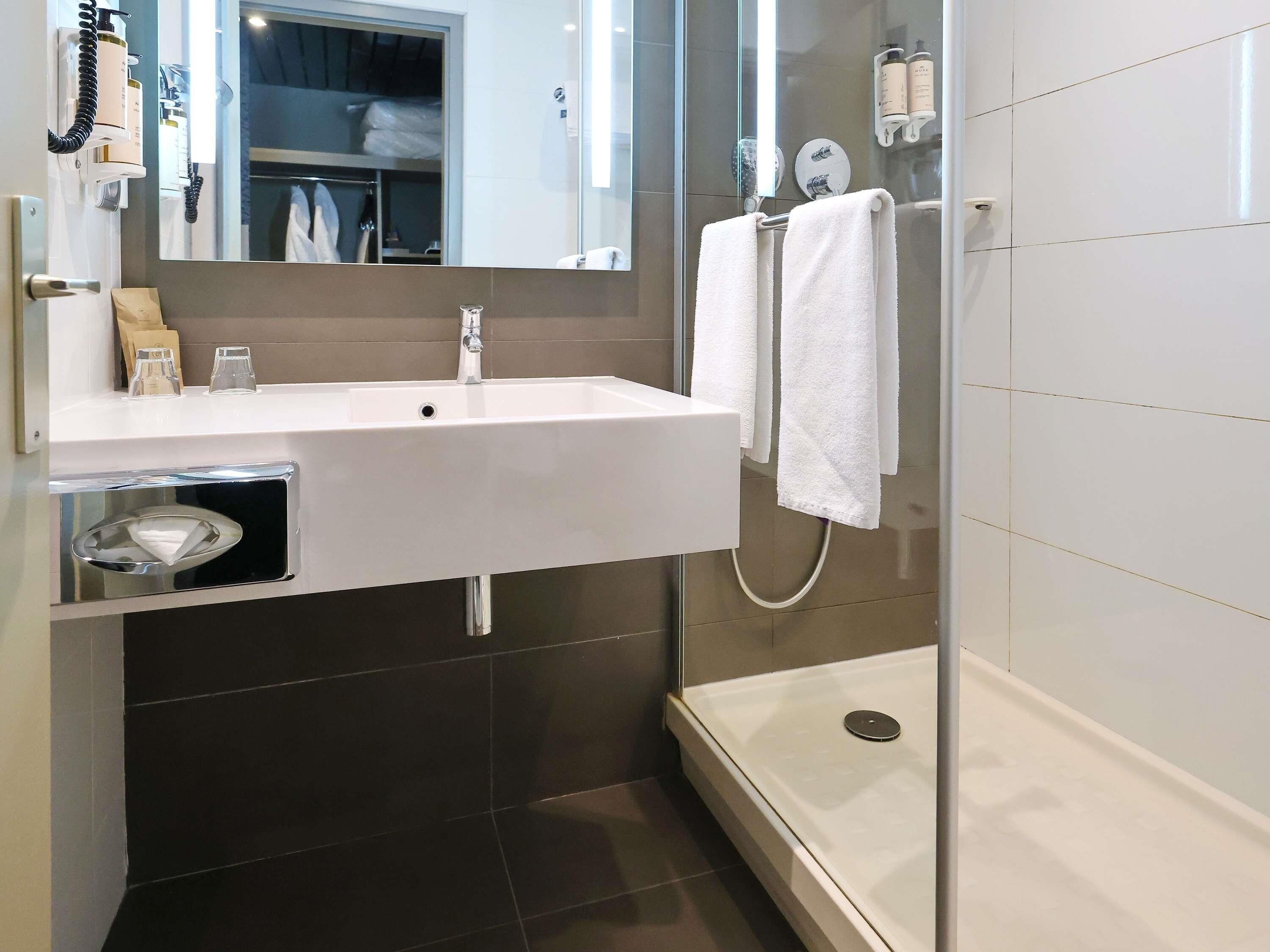 Une salle de bain moderne avec un lavabo blanc, une douche en verre et un miroir au-dessus du lavabo.