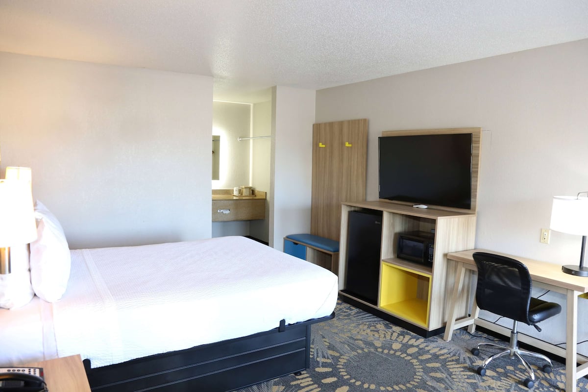 A hotel room with a bed, a desk, a chair, a television, and a wardrobe.