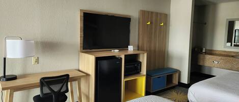 Una habitación de hotel con escritorio, silla, televisor, minibar y dos camas.