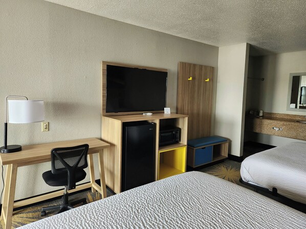 A hotel room with a desk, chair, television, minibar, and two beds.