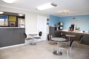 A clean, well-lit indoor space with a reception desk, two round tables with chairs, a coffee machine, and a counter with a coffee dispenser. - Days Inn by Wyndham Monroe LA (Monroe)
