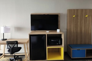 A compact room with a desk, a chair, a television, a microwave, and a wardrobe.
