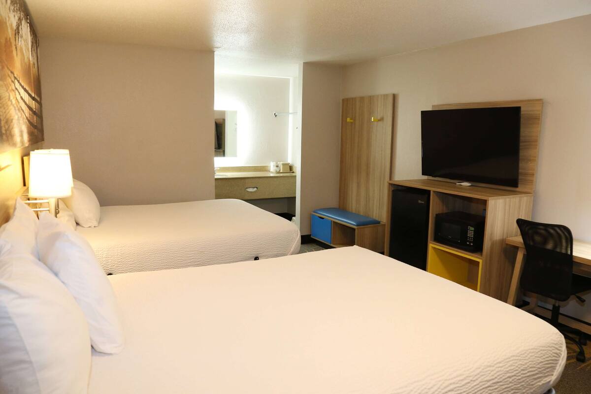 A hotel room with two beds, a television, a desk with a chair, and a microwave.