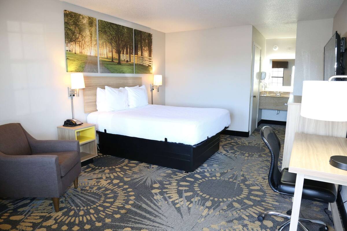 A hotel room with a large bed, a chair, a desk, and a painting on the wall.