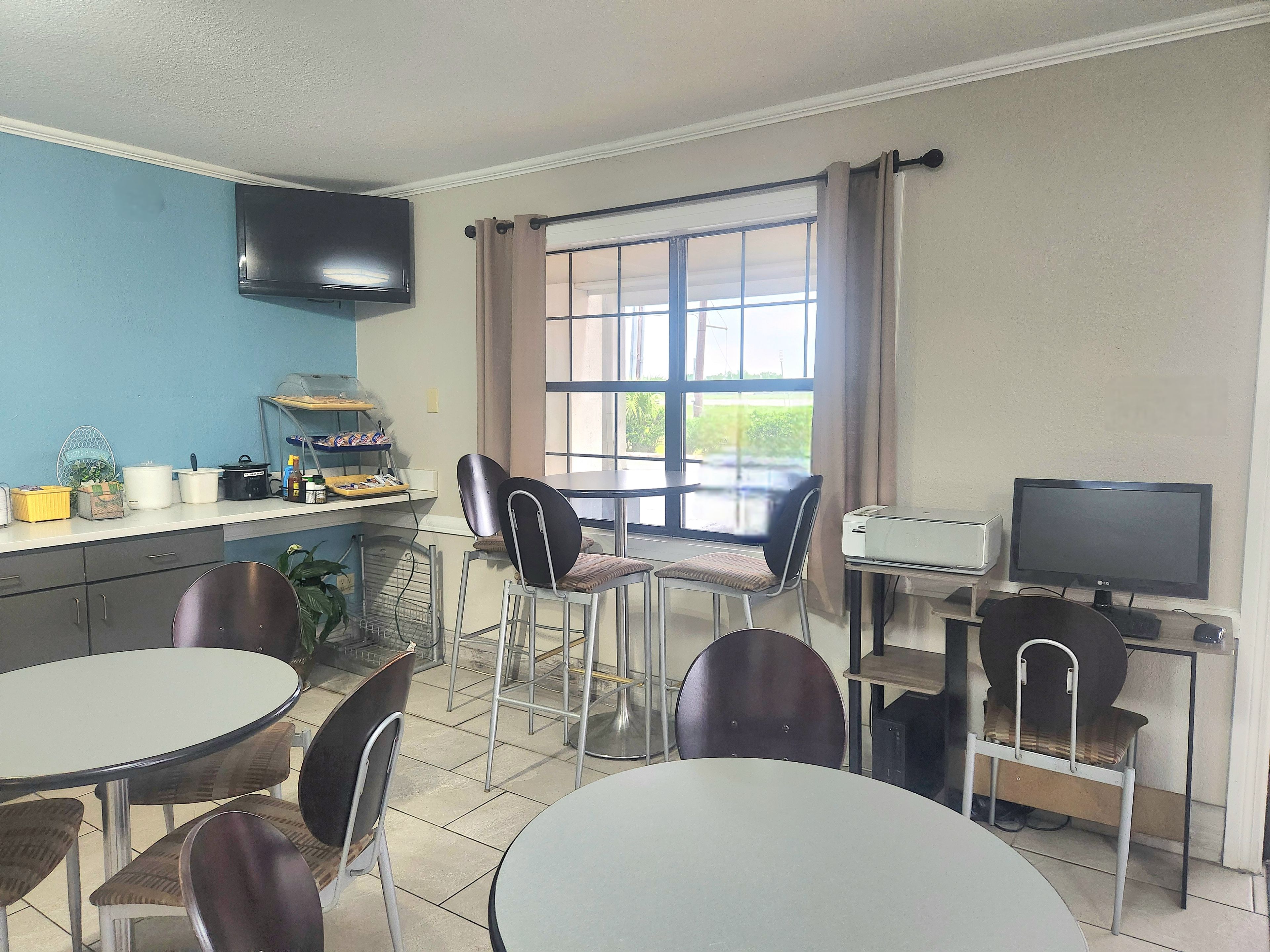 A room with a dining area, a kitchen counter with appliances, a television, and a window with curtains.