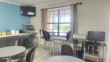 A room with a dining area, a kitchen counter with appliances, a television, and a window with curtains.