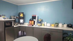A compact kitchen with a microwave, coffee machine, and a water dispenser. There is a small dining table with two chairs. - Days Inn by Wyndham Monroe LA (Monroe)